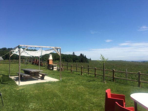 Vaste prairie verte avec un abri, des chaises rouges et un ciel bleu dégagé.