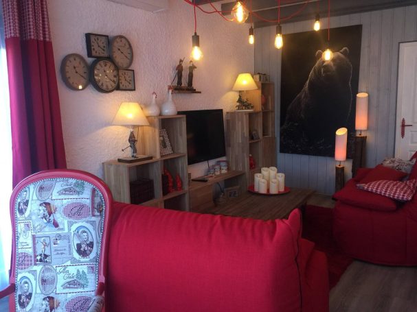 Salon cosy avec canapés rouges, étagères en bois, lampes et décor chaleureux.