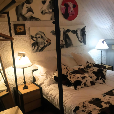 Chambre avec lit à baldaquin, décorée de vaches et éclairage doux.