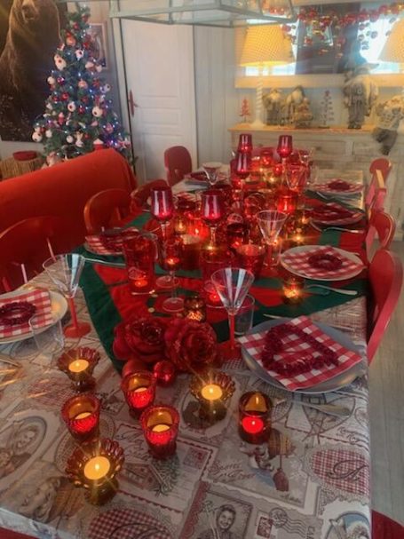 Table de fête décorée avec assiettes, bougies et un sapin de Noël en arrière-plan.