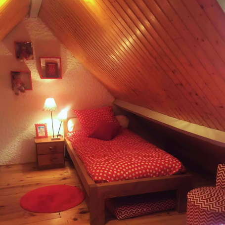 Chambre mansardée avec lit, décor rouge à pois et éclairage doux.